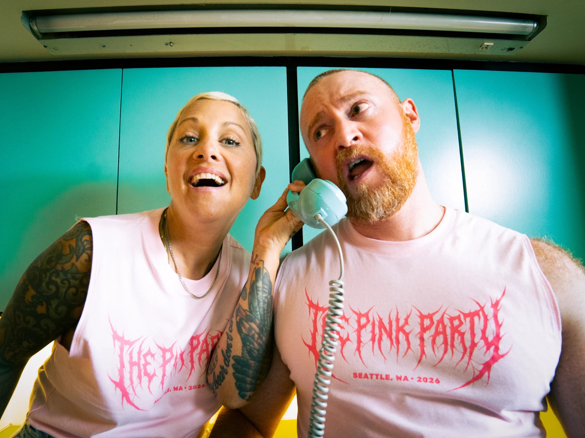 Two people wearing 'The Pink Party' shirts in a room with teal walls.