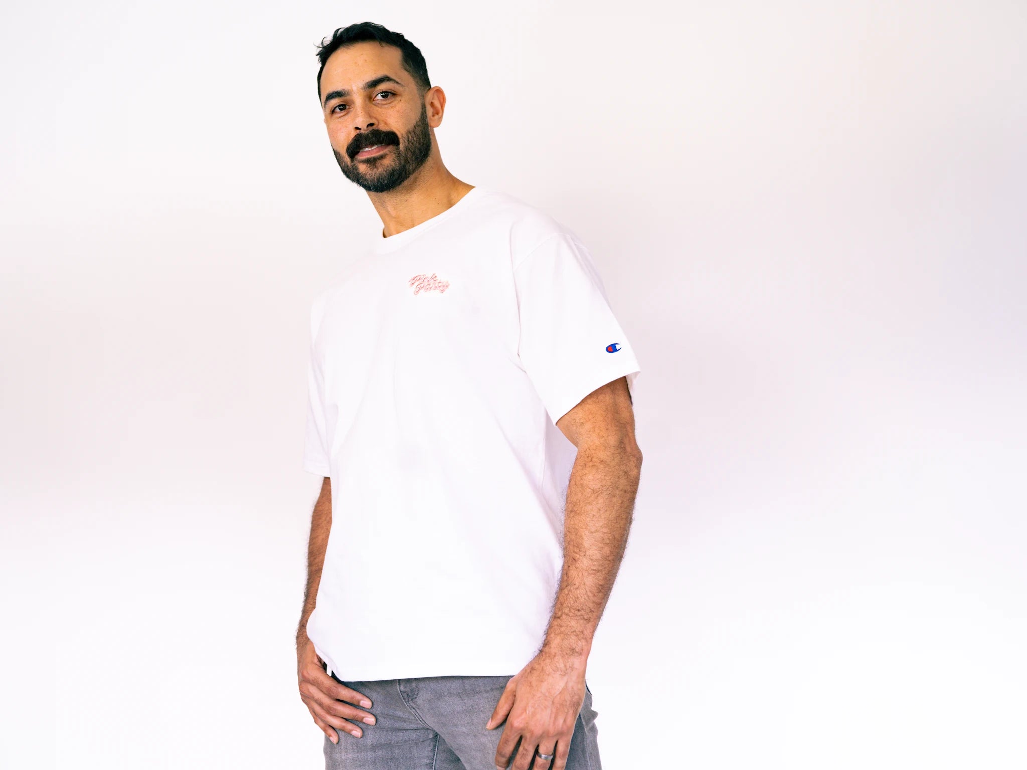 Man wearing a white t-shirt with a small logo on a plain background