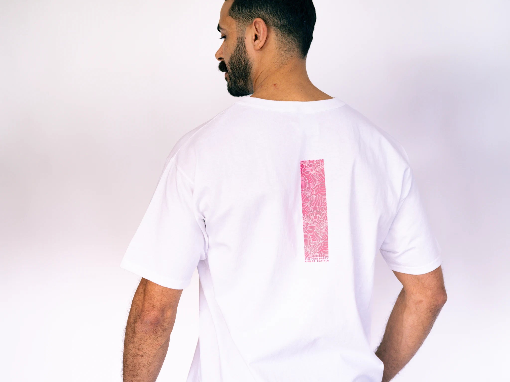 Man wearing a white t-shirt with a pink rectangle on the back against a plain background