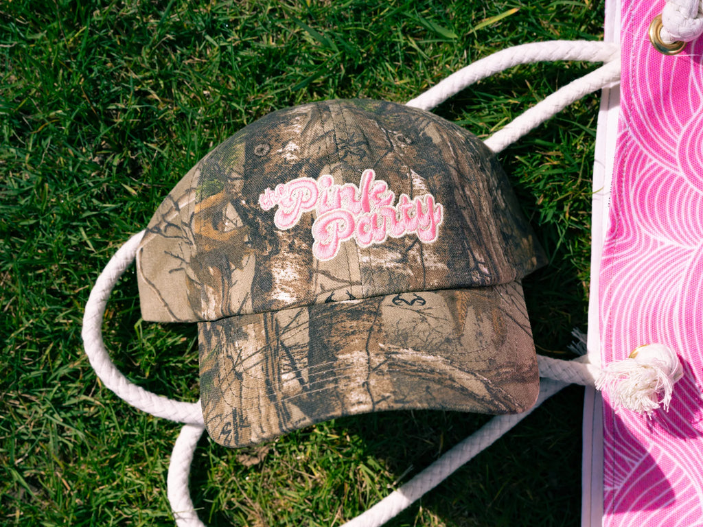 Camouflage-patterned cap with 'Pink Party' text on grass