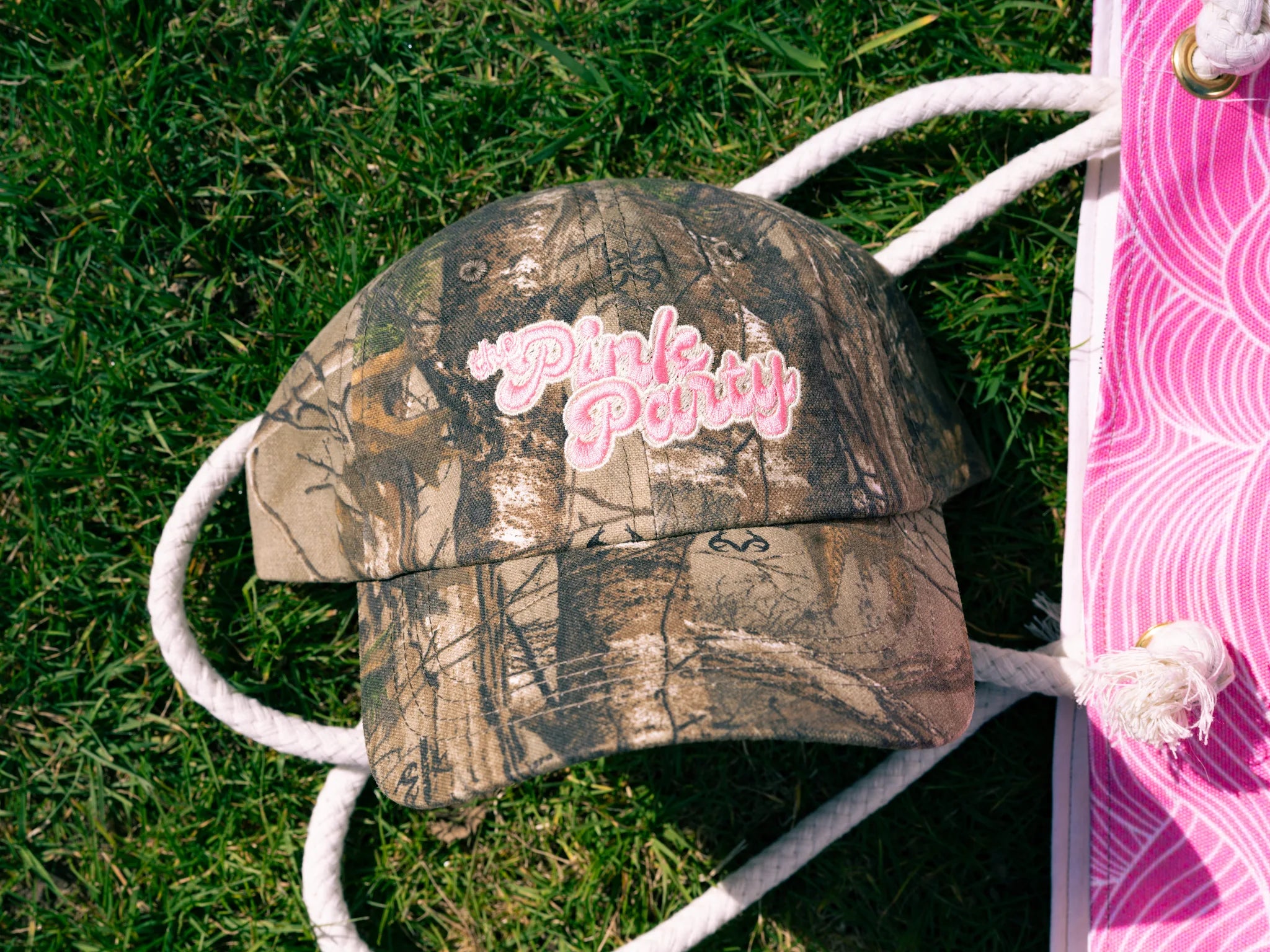 Camouflage-patterned cap with 'Pink Party' text on grass
