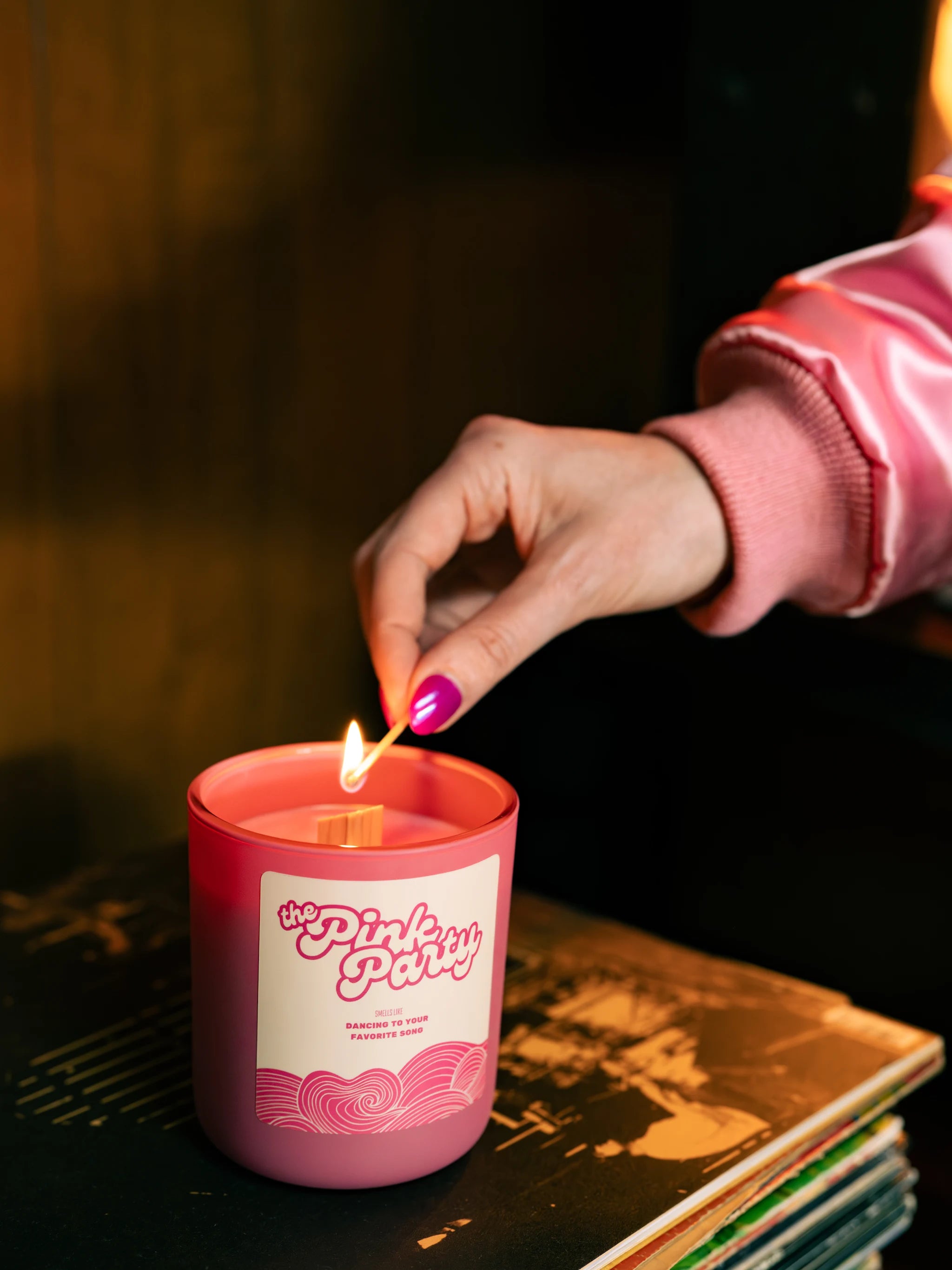 Person lighting a pink candle labeled 'The Pink Party' with a dark background