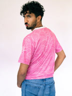 Man wearing a pink patterned t-shirt and blue jeans against a white background