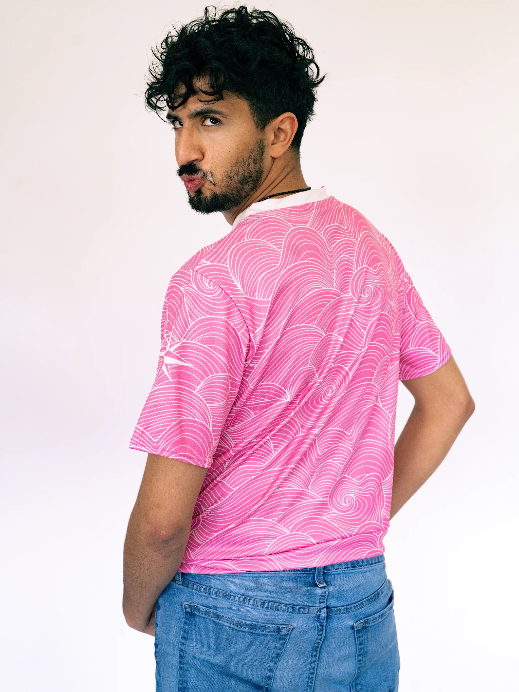 Man wearing a pink patterned t-shirt and blue jeans against a white background
