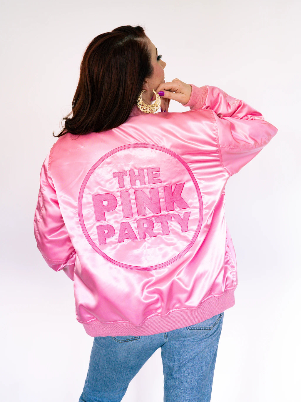 Back view of a shiny pink satin bomber jacket with The Pink Party embroidered in a circle on the back.