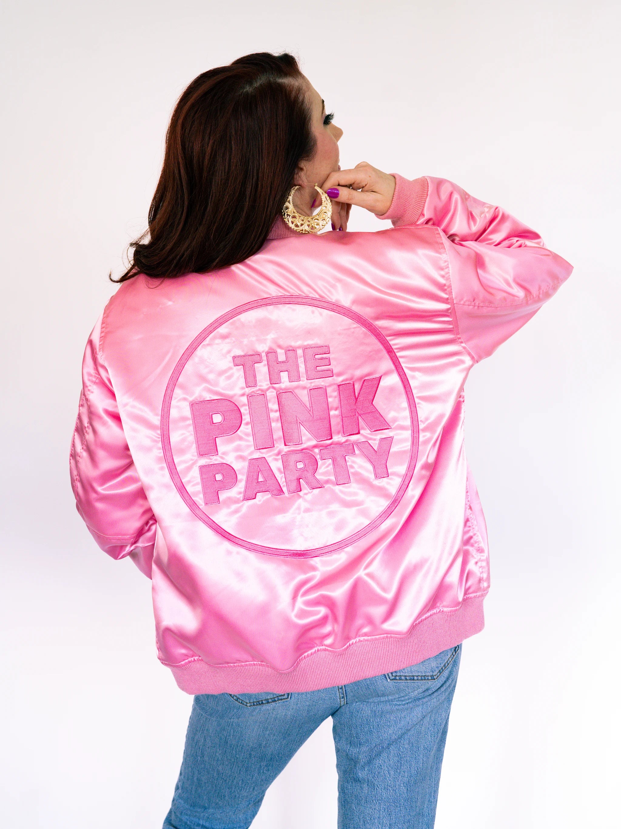 Back view of a shiny pink satin bomber jacket with The Pink Party embroidered in a circle on the back.