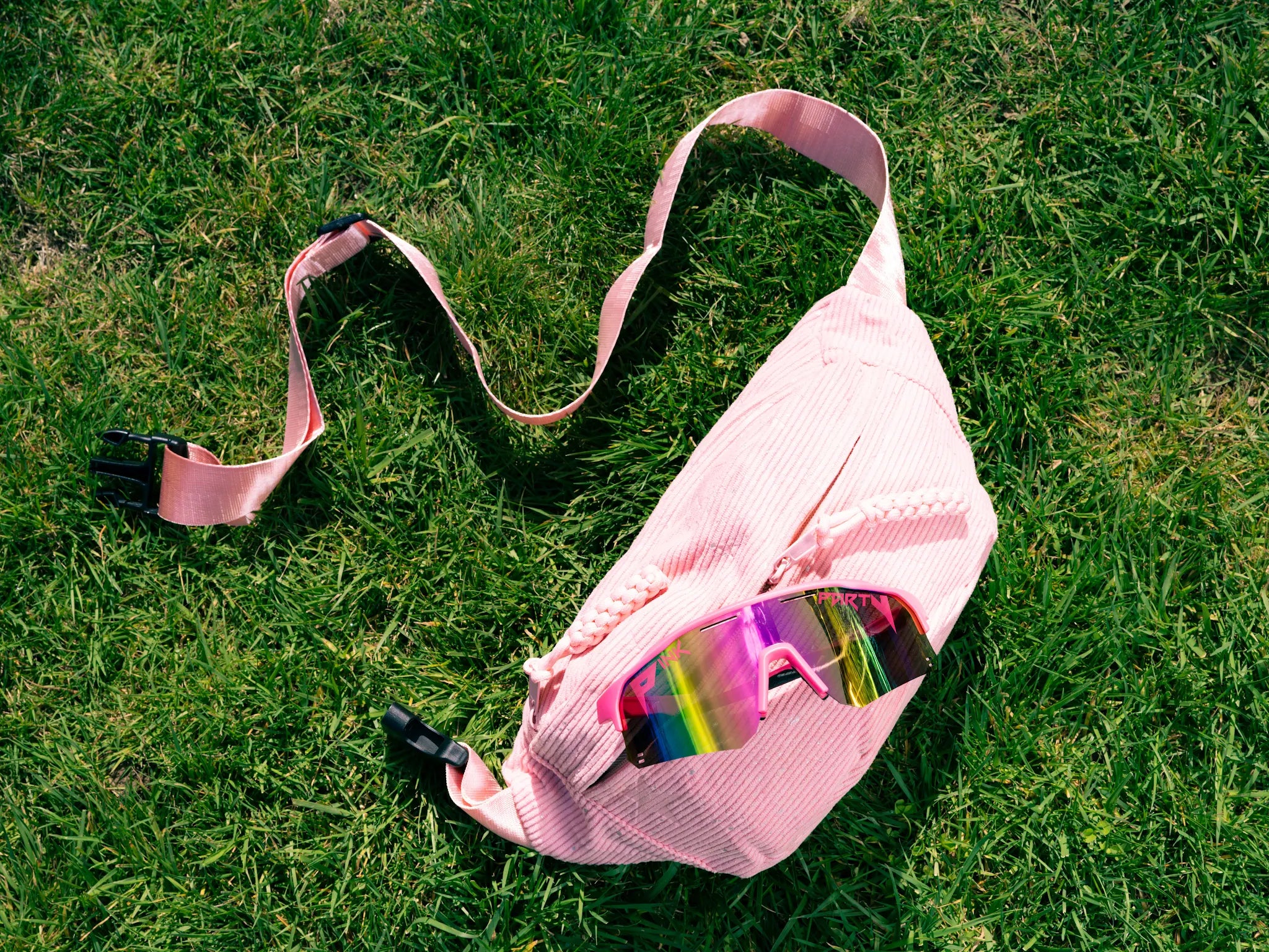 Pink waist bag with sunglasses on grass