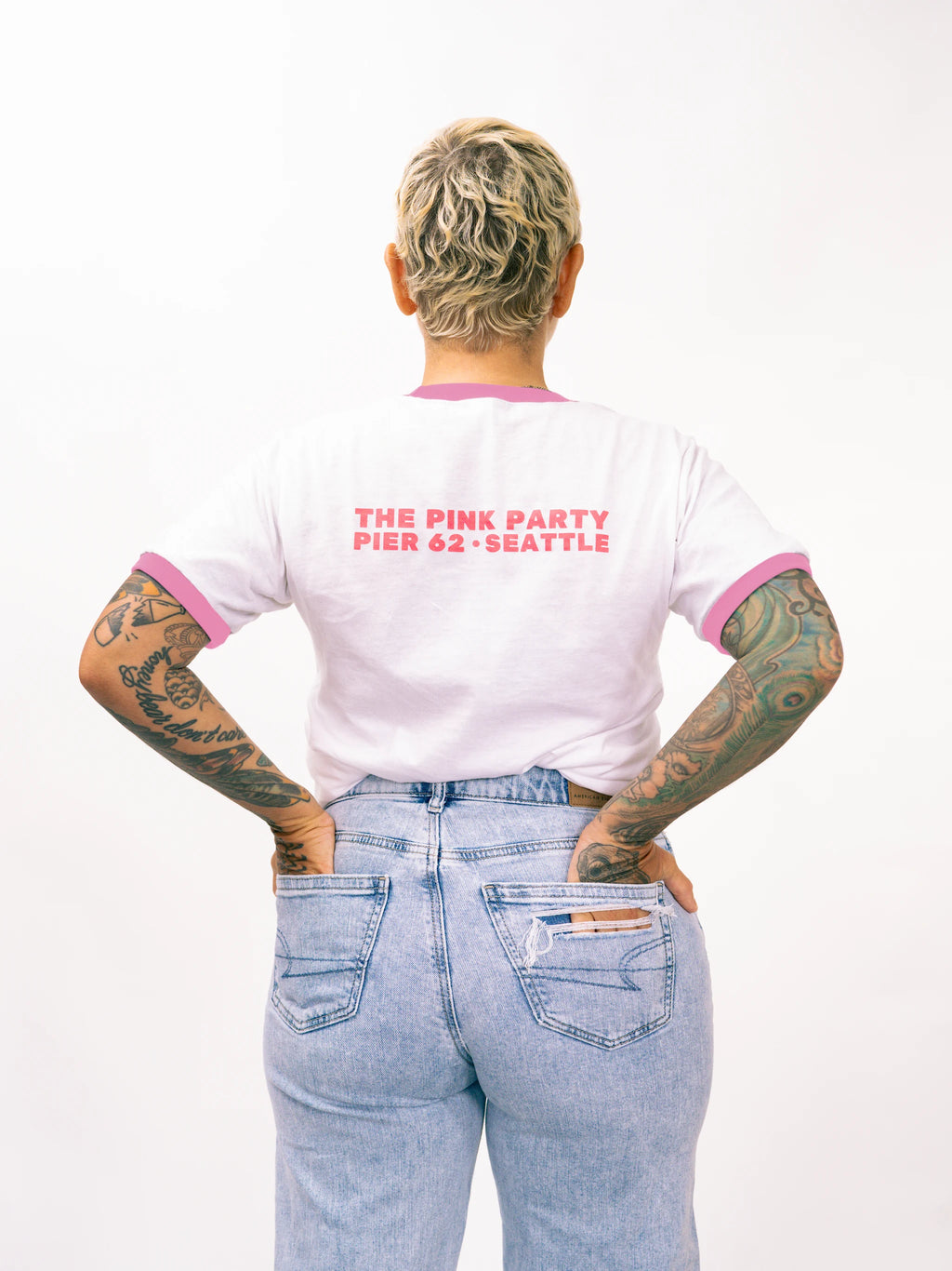 Person wearing a white t-shirt with pink trim and text, standing against a white background