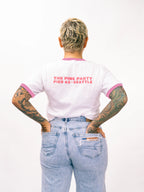 Person wearing a white t-shirt with pink trim and text, standing against a white background