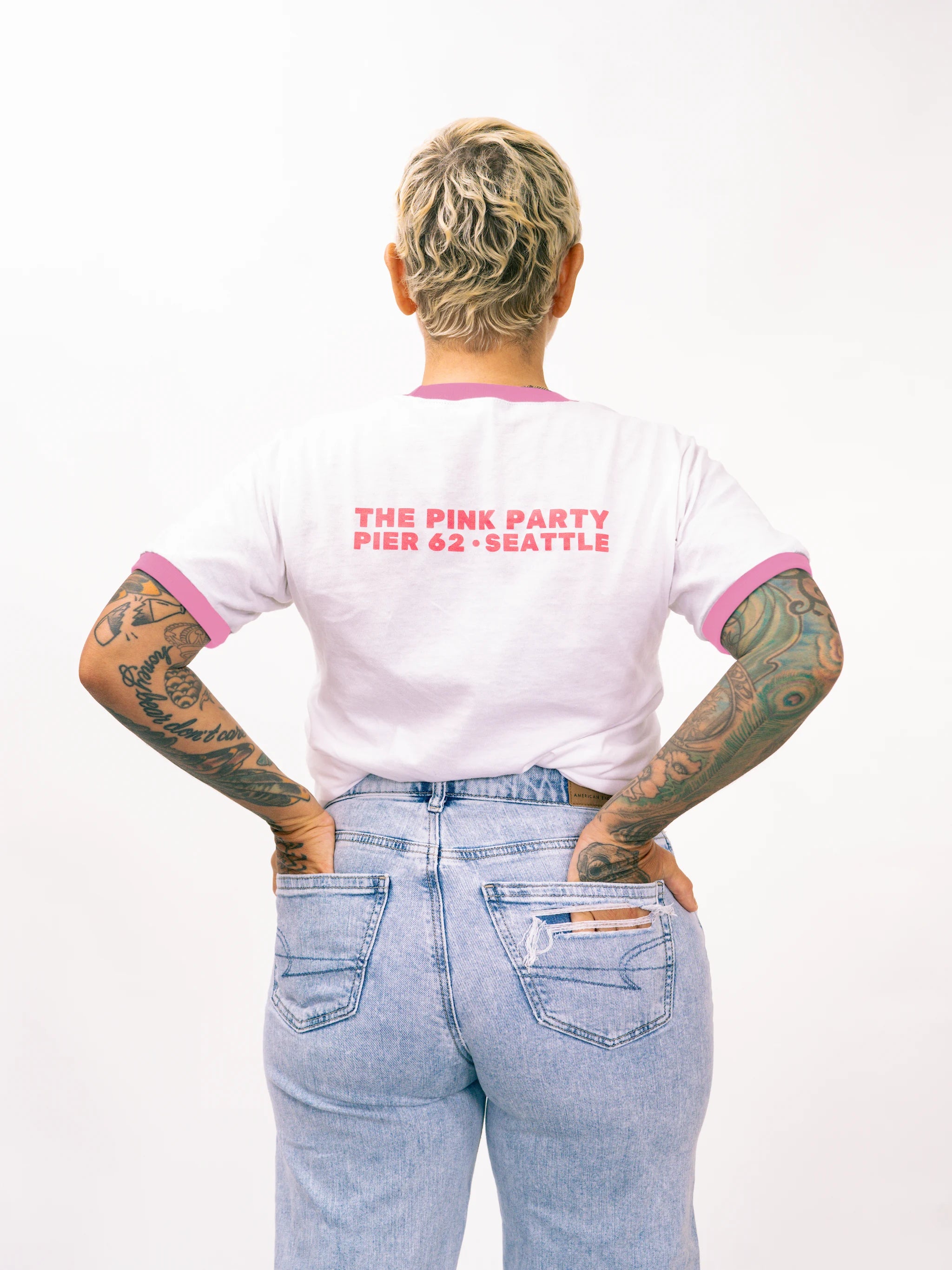 Person wearing a white t-shirt with pink trim and text, standing against a white background