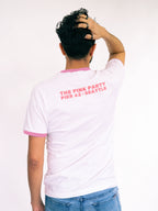 Person wearing a white t-shirt with pink text on the back, standing against a plain background