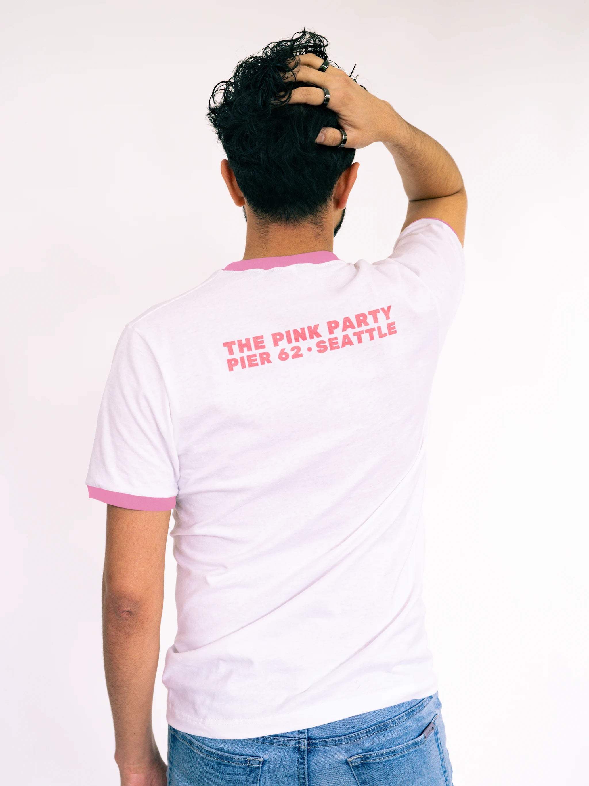 Person wearing a white t-shirt with pink text on the back, standing against a plain background