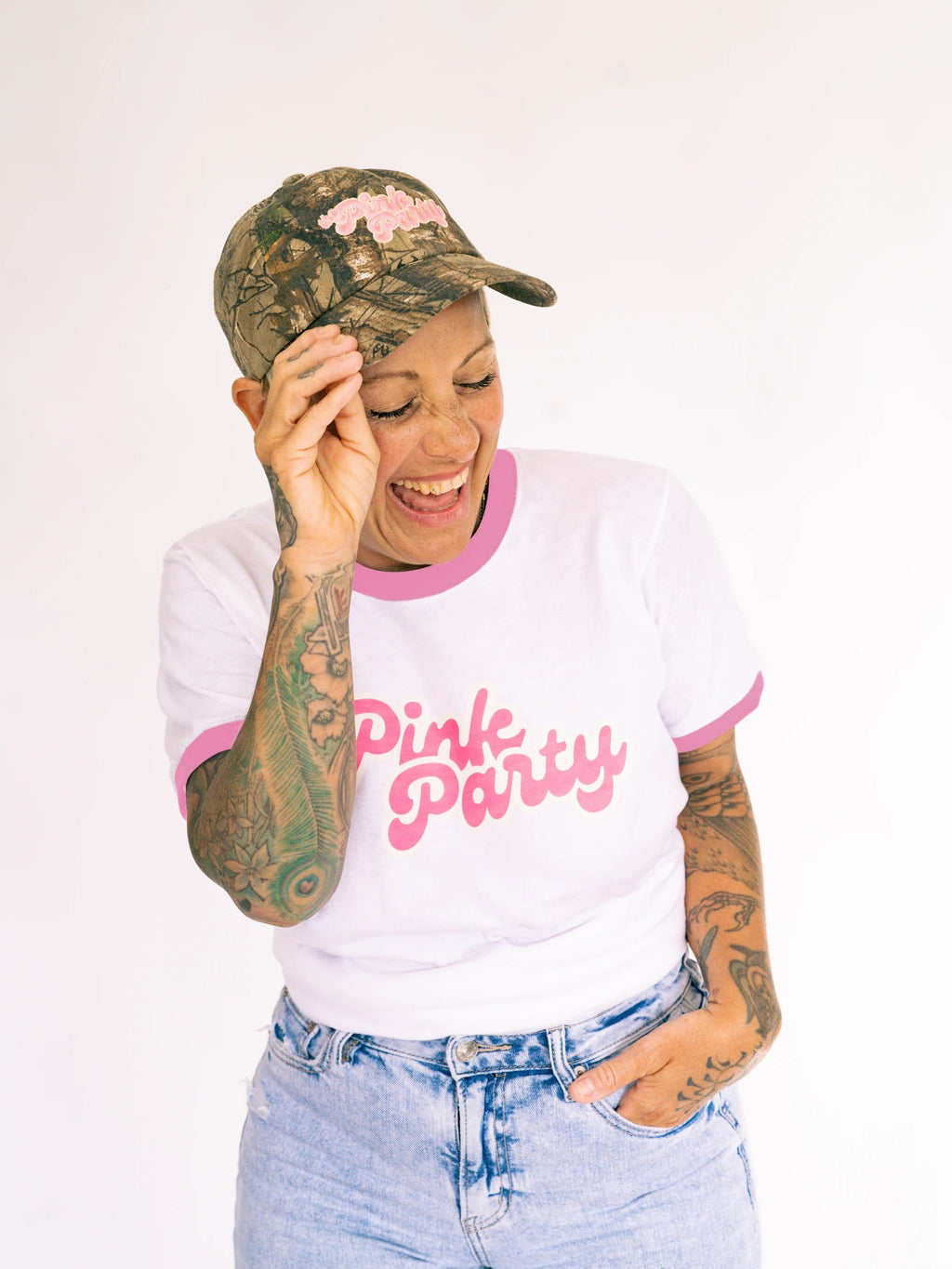 Person wearing a white t-shirt with 'Pink Party' text, camouflage cap, and denim shorts on a white background